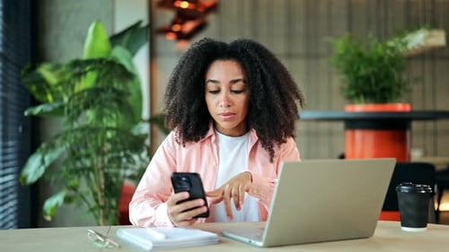African American Woman Working Online with Smartphone Laptop in Modern Office