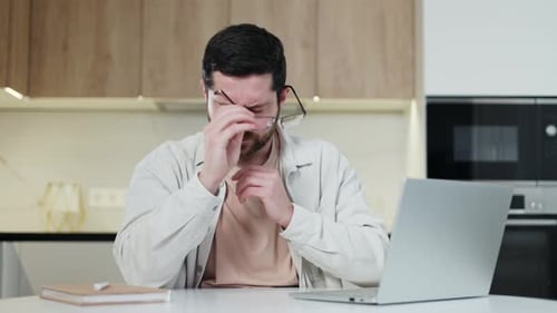 Man Working on Laptop Rubs Eye, Takes Break