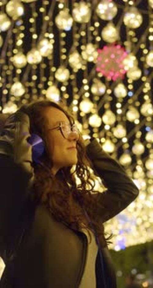 Vertical Footage of a Young Woman Dances on the Street at Night in the Light of Festive Lights on