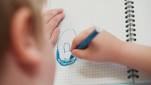 Child Drawing with Blue Marker on Notebook