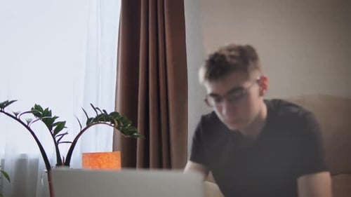 Young Man Using Laptop Sitting on Couch at Home