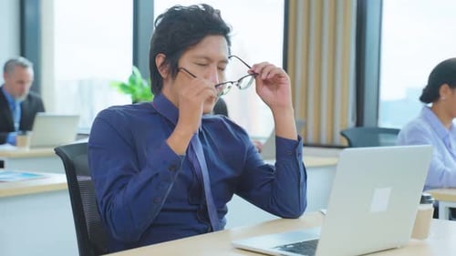 Exhausted Asian business man using laptop computer working in office.