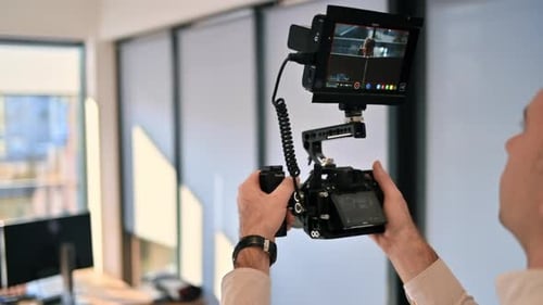 Professional photographer holding a camera with external display. Shooting a man at work in an offic