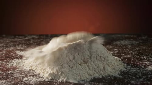 Dough falls on flour creating a splash, slow motion, side view