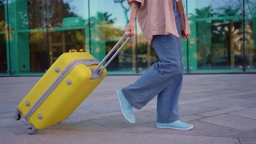 Closeup of a Suitcase Yellow Rolling Against the Background of a Modern Airport Building