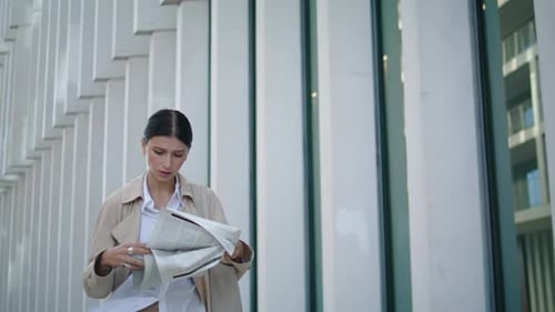 Attractive businesswoman reading newspaper walking to work in modern city