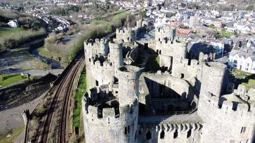Train travelling railway tracks alongside medieval Conwy castle Welsh market town ruins aerial view