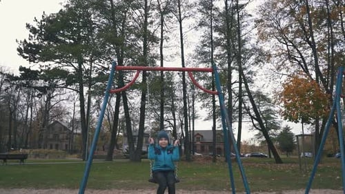 Happy Boy is Swaying on Swing in Park at Autumn Day and Jumping Out in Slow Motion. A Boy Riding on