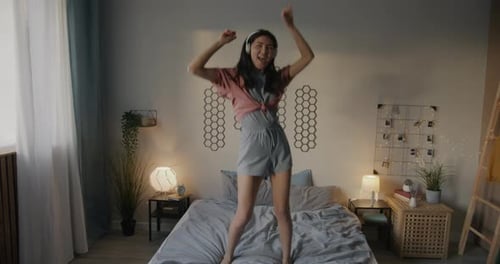 Woman Dancing on Bed with Headphones in Bedroom
