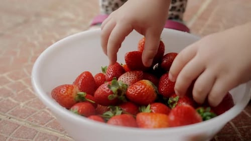 Children's Hands Take Strawberries From a White Plate on the Street