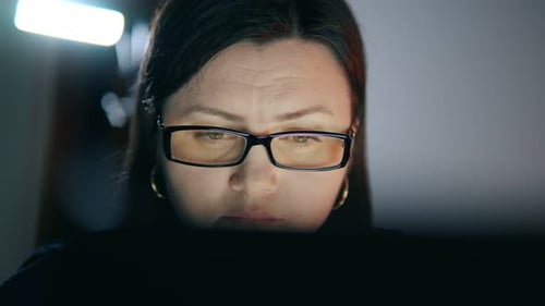 Brunette Woman with Glasses Working Late at Night in Front of a Computer at Home