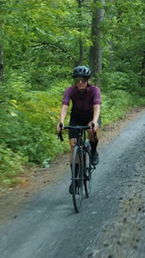 Female cyclist in helmet and sunglasses riding on gravel bicycle. Vertical video