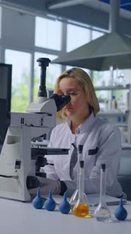 Woman Scientist Using Microscope in Lab with Beakers
