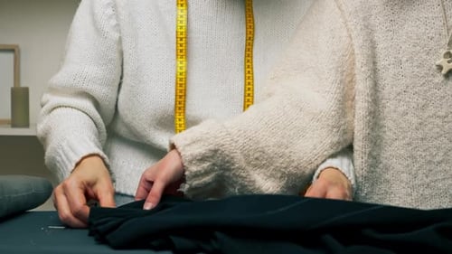 Nahaufnahme in einer Nähwerkstatt Zwei Näherinnen legen schwarzen Stoff entsprechend der Form aus