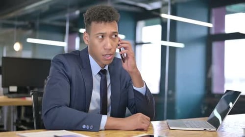 Young Businessman Talking on Smartphone and Working on Laptop