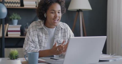 African American Woman Making Online Video Call Using Wireless Earphones and Laptop in Office