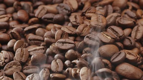 Los granos de café giran y se produce un ligero humo tostado.