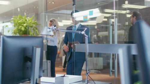 In the Big Office Businessman Walks into Glass Office and Shows Tablet Computer to His Colleague .