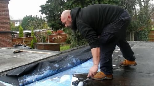 Man Applies Waterproofing to Roof With Roller
