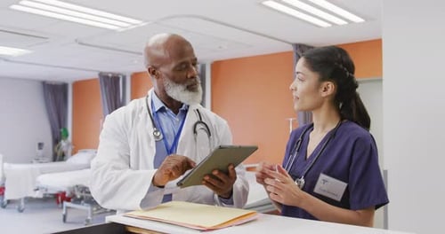 Diverse male and female doctors using tablet and talking at hospital