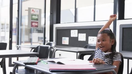 In a school classroom, a young African American girl raises her hand eagerly with copy space