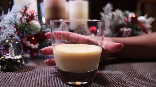 A female hand reaching for a glass of Christmas eggnog with cinnamon being added