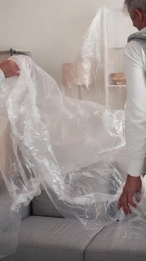 Couple Covering Gray Couch With Plastic Wrap