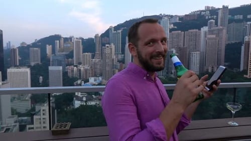 Handsome young man enjoys refreshing beer at rooftop skybar view in slow motion
