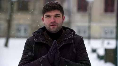 Man Rubs Hands Together in Snowy Urban Park
