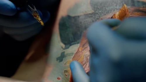 Tattoo Artist Wearing Blue Gloves Operates a Tattoo Machine Skillfully Drawing Precise Lines on a