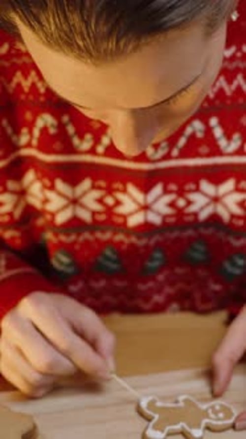 Vertical video. Using a Toothpick, She Carefully Adds Icing Details to a Gingerbread Man Cookie, Hig