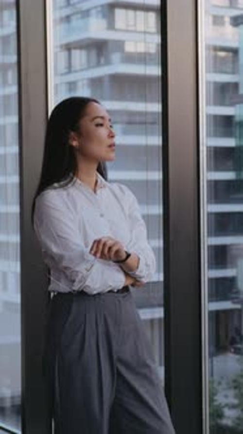 Young Businesswoman Stands By Office Window Gazing at City