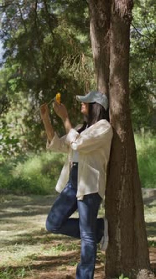 Young Woman Leans on Tree Holding a Flower