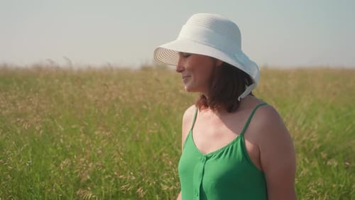 Young Woman Walking Through Barley Field in Green Dress and Sunhat
