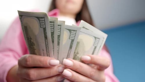Close-up off female hands counting a stack of hundred-dollar US banknotes
