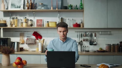 Trabajador remoto tomando café trabajando en una computadora portátil desde casa