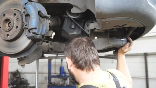 Auto Mechanic Installing Part to Car at Garage or Service Professional Repairman Working Underneath
