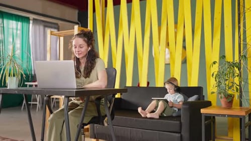 Woman Working on Laptop While Child Uses Tablet