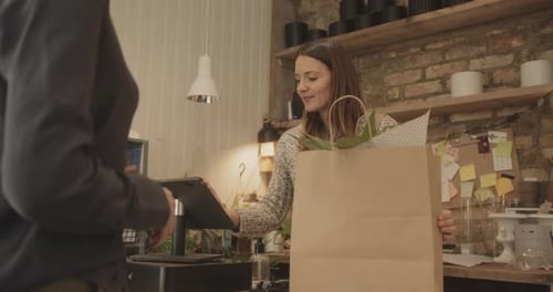 Retail clerk giving paper shopping bag with purchase to customer in store