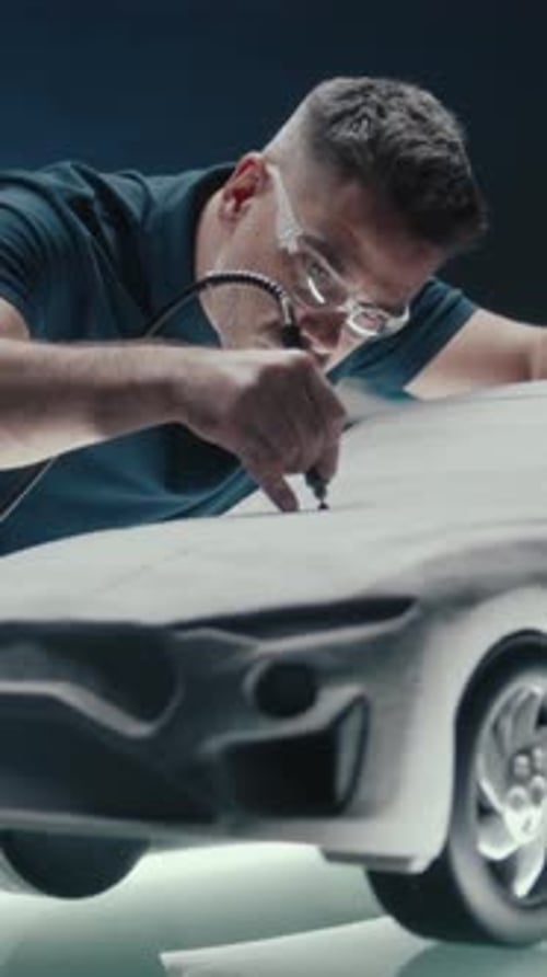 Un designer automobile senior travaille sur un prototype de sculpture en argile pour voiture à l'aide d'un outil rotatif
