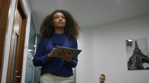 African american executive woman walks office hallway analyzing corporate data on tablet
