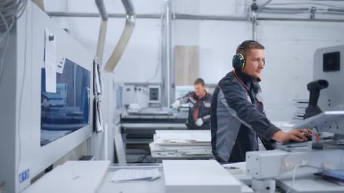 Arbeiter in Uniform und schützenden Kopfhörern verarbeiten Spanplatten mit Furnier in einer Fräsmaschine