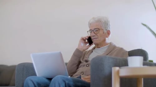 Älterer Mann schaut beim Telefonieren auf den Laptop-Bildschirm