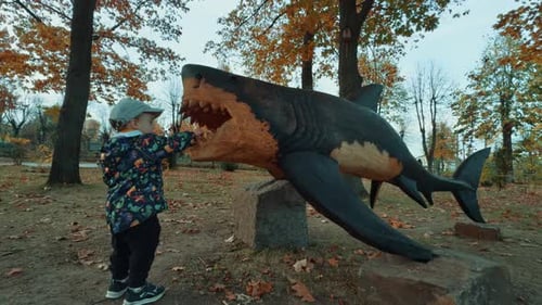 Caucasian toddler playing at the life-size wooden sculpture of a shark. in the park.