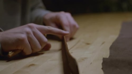 Les mains tirent et façonnent un bracelet en cuir marron sur une surface de travail en bois