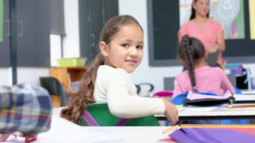 In school, girl smiling and holding book in classroom, sitting at desk