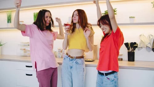 Três amigos organizam uma festa em casa em sua cozinha moderna bebendo vinho e dançando ao som da música The