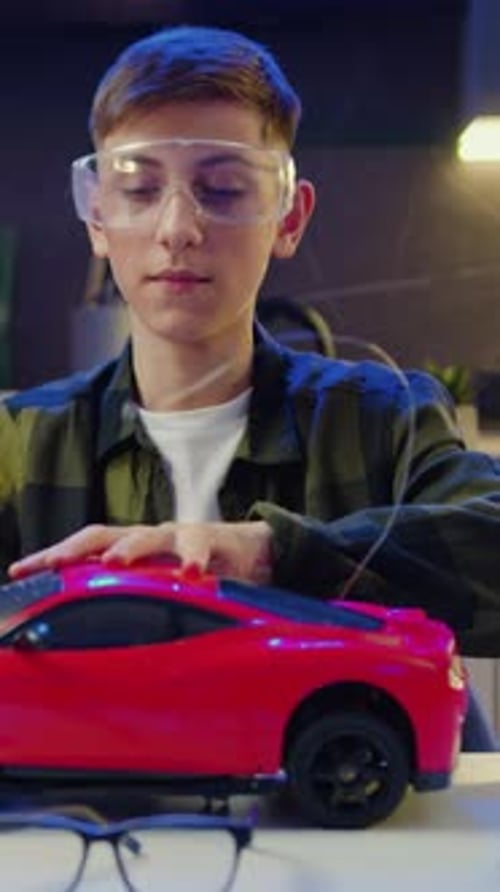 Teen Repairs Toy Car Under Smartphone Camera at Desk