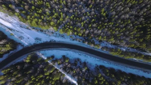 Aerial winter road curve through snowy forest landscape with one car driving
