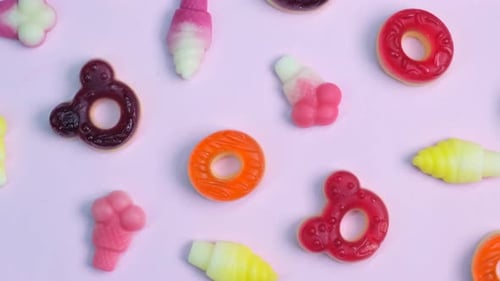 Rotationshintergrund mit verschiedenen Gelee-Bonbons, Bären, Donuts, Bonbons auf rosafarbenem Hintergrund, Nahaufnahme